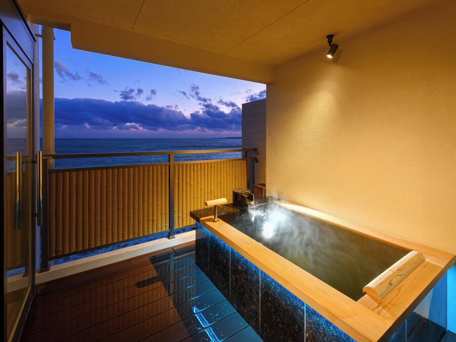 Zona de spa con hidromasaje, suelo de madera, vista al océano y balcón con barandilla.