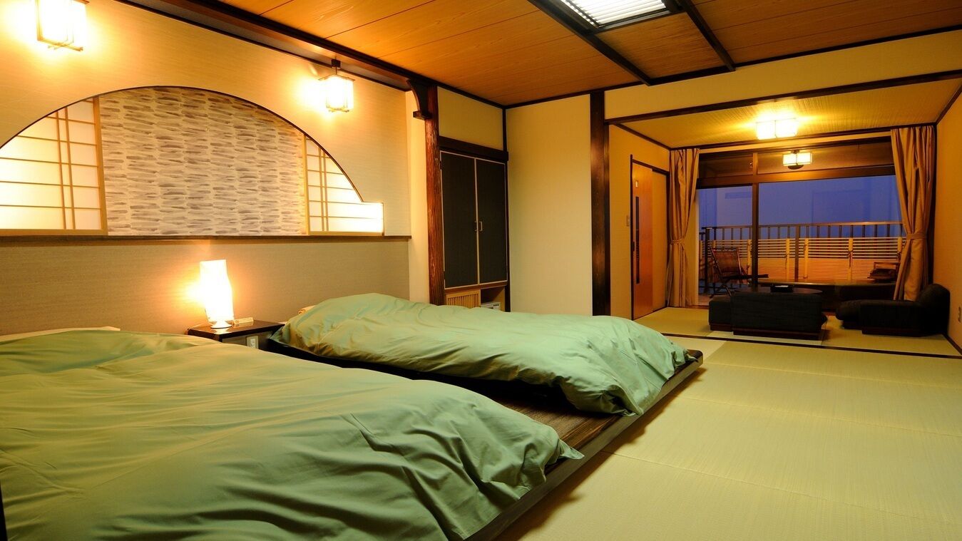 A room with two beds, a wooden ceiling, a view of the outside, and a sliding door leading to a balcony.