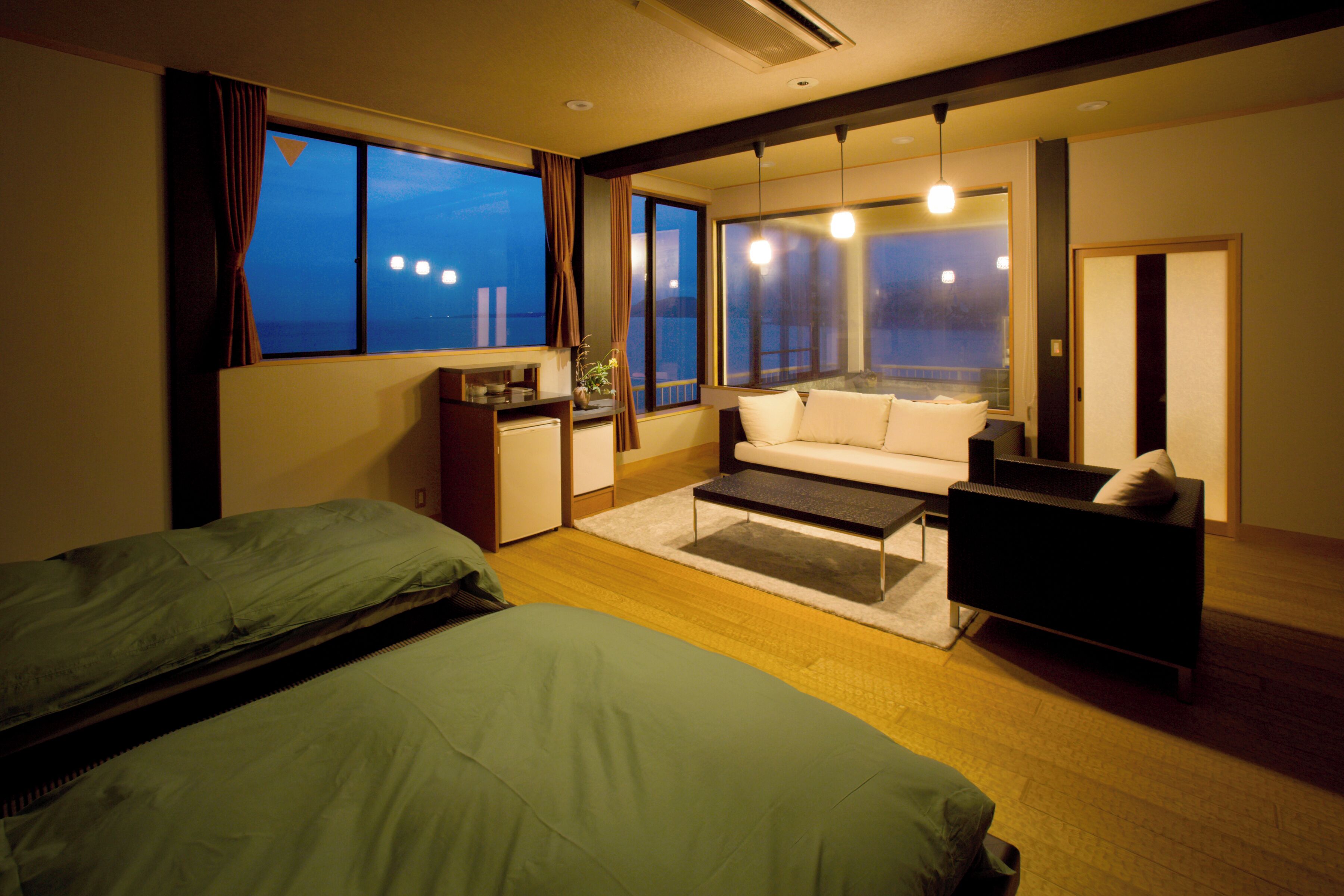 A hotel room with a bed, a sofa, a coffee table, and a desk with a lamp.