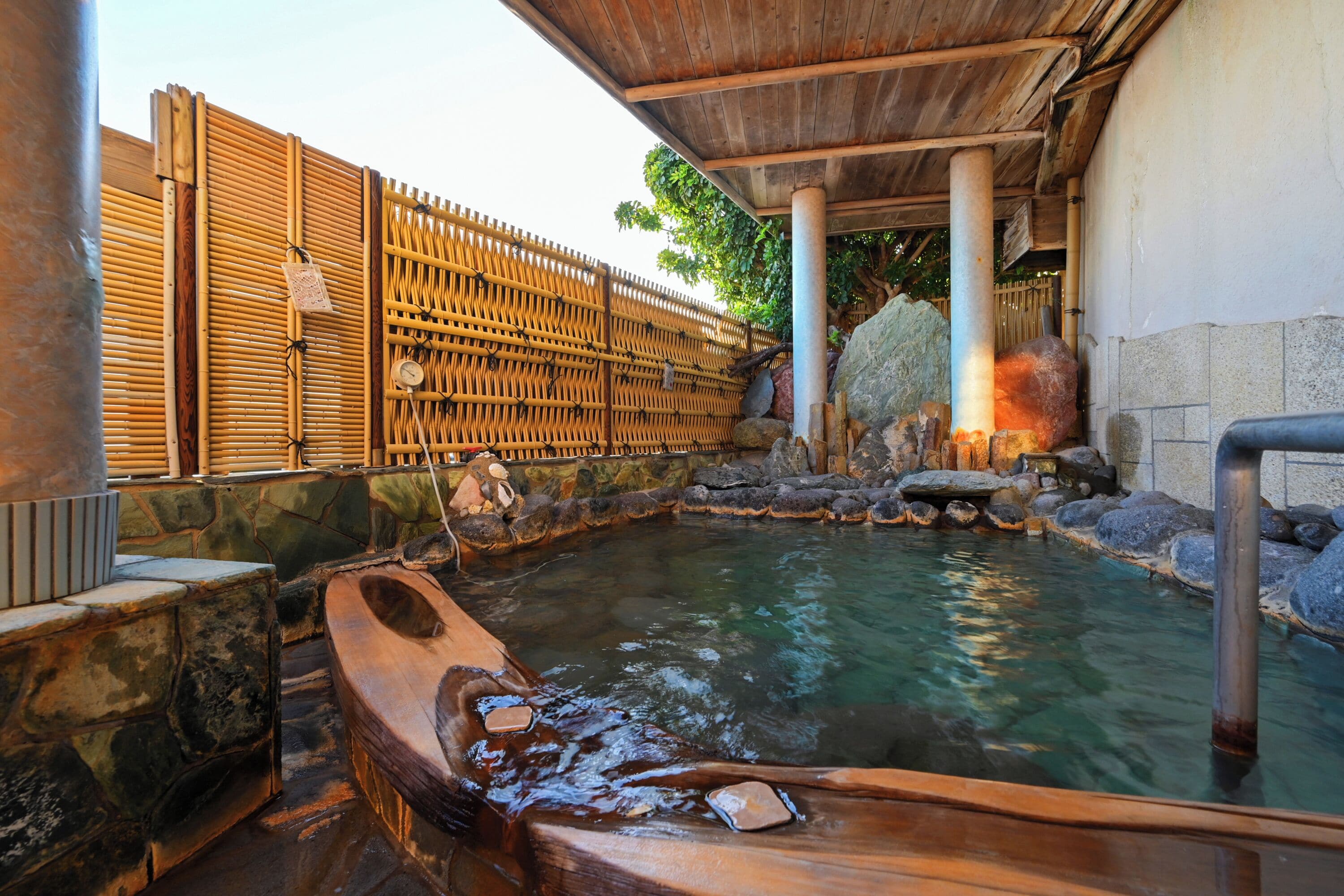 Ein traditionelles japanisches Onsen mit Holzbad, Steinwänden und einem Bambuszaun.
