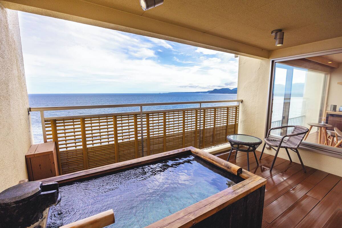 A balcony with a view of the sea, a hot tub, and outdoor furniture.