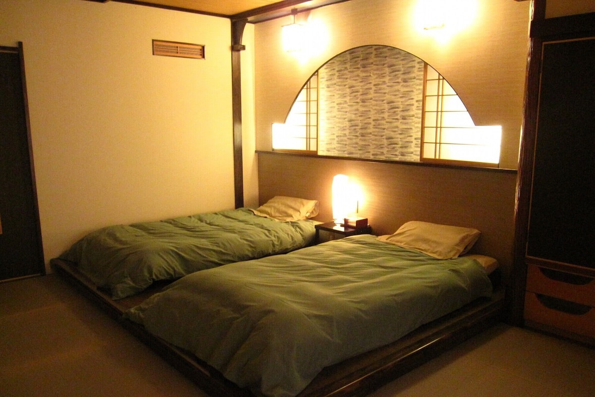 A small, dimly lit room with two single beds, a nightstand with a lamp, and a decorative wall arch.