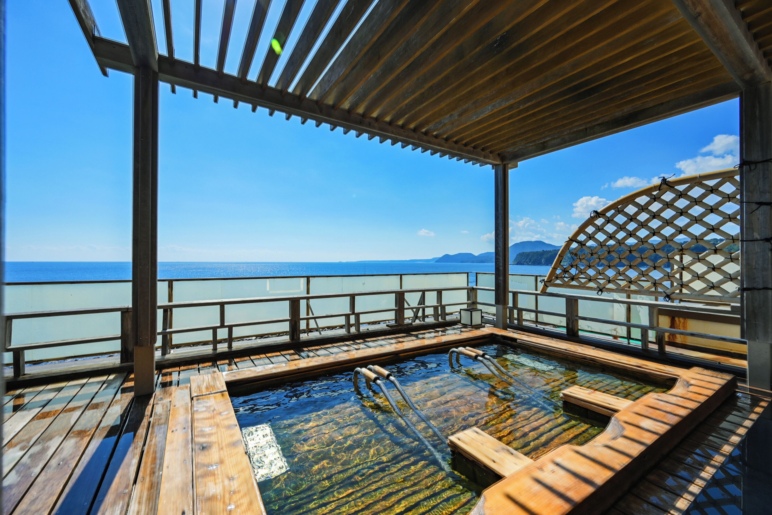 A wooden deck with a hot tub, wooden seating, and a view of the sea.
