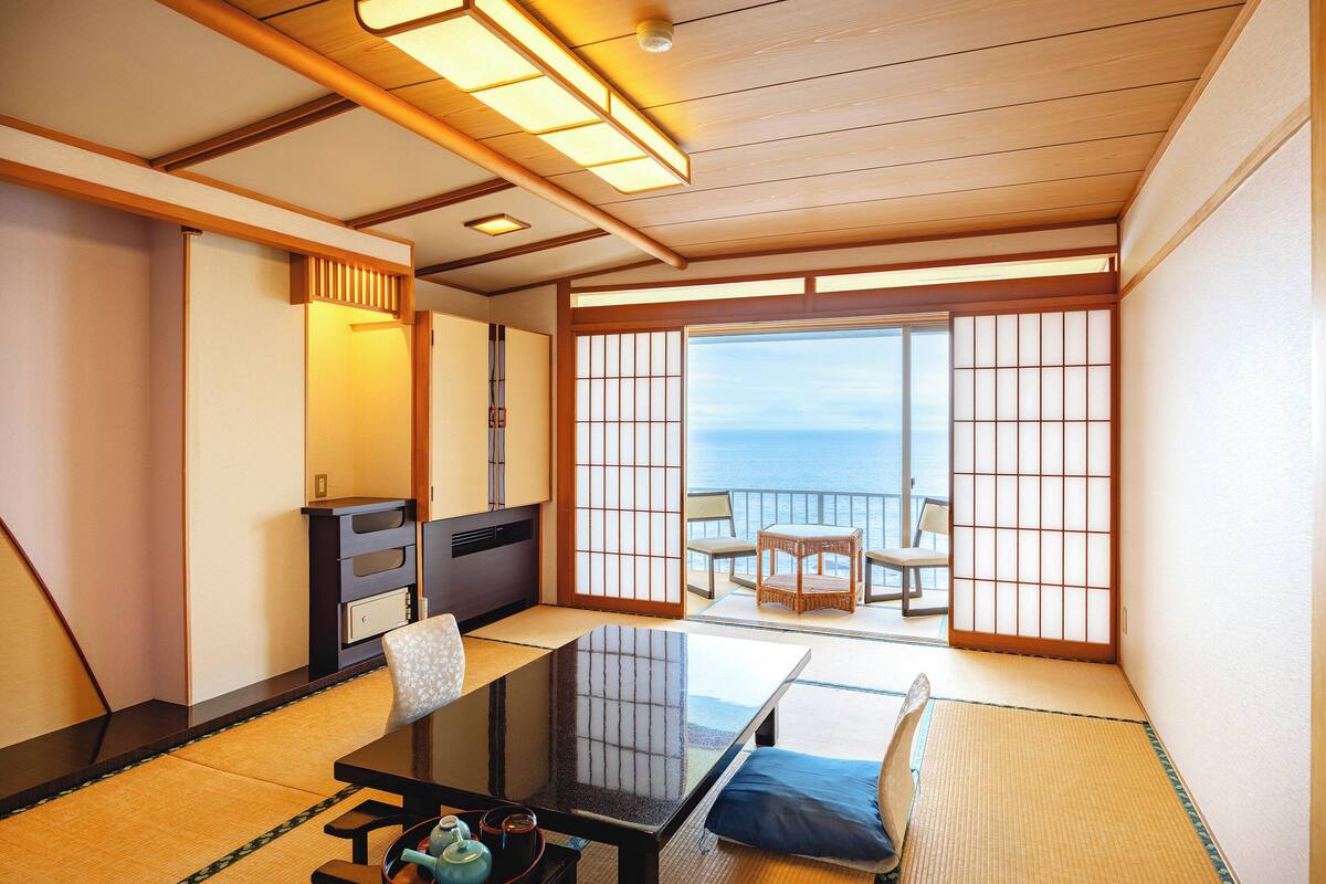 A traditional Japanese room with tatami flooring, a low table, and sliding doors leading to a balcony with a view.