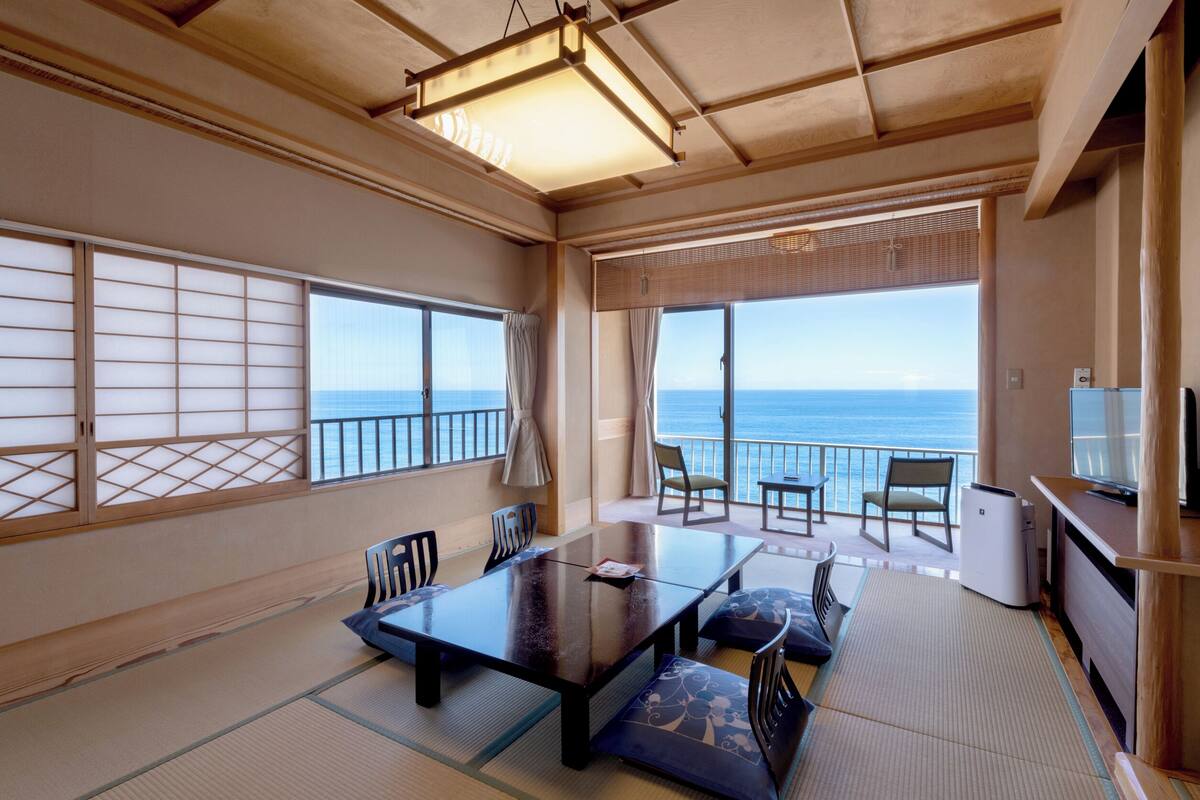 A traditional Japanese-style room with tatami flooring, a low table, and a view of the sea.