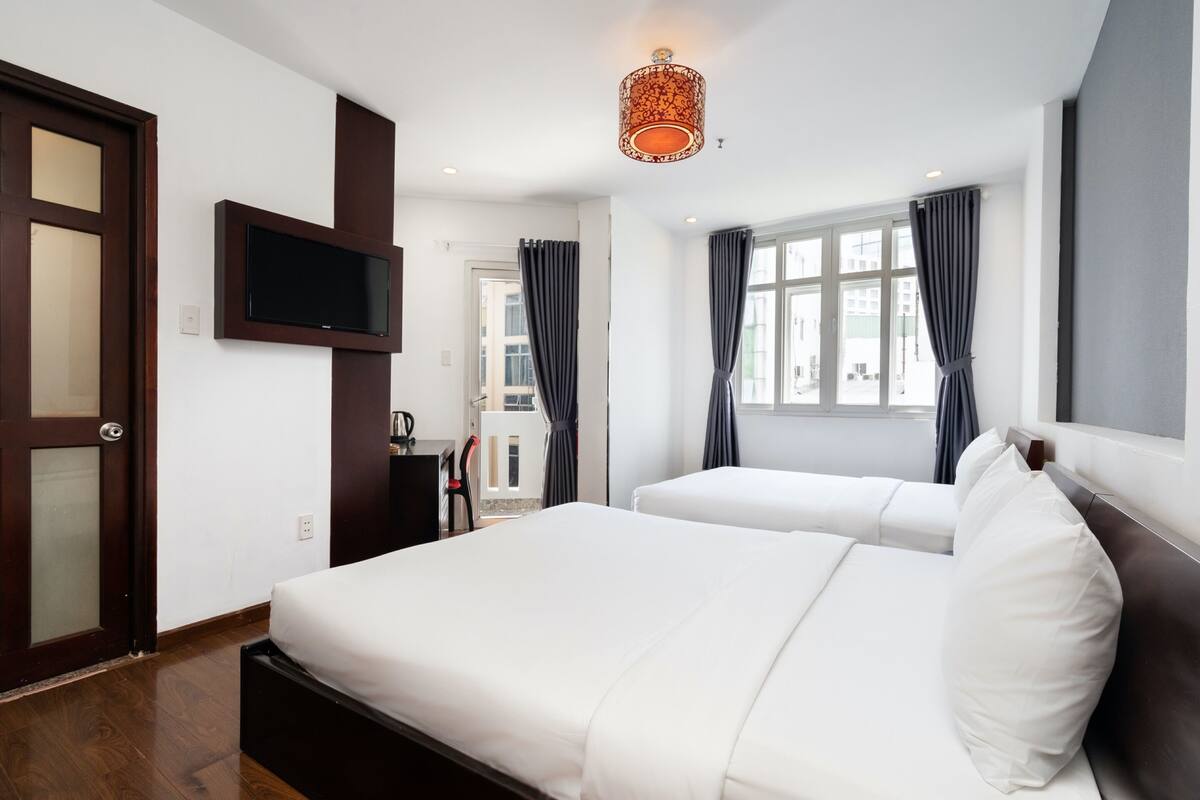 A hotel room with two beds, a TV mounted on the wall, and a window with curtains.