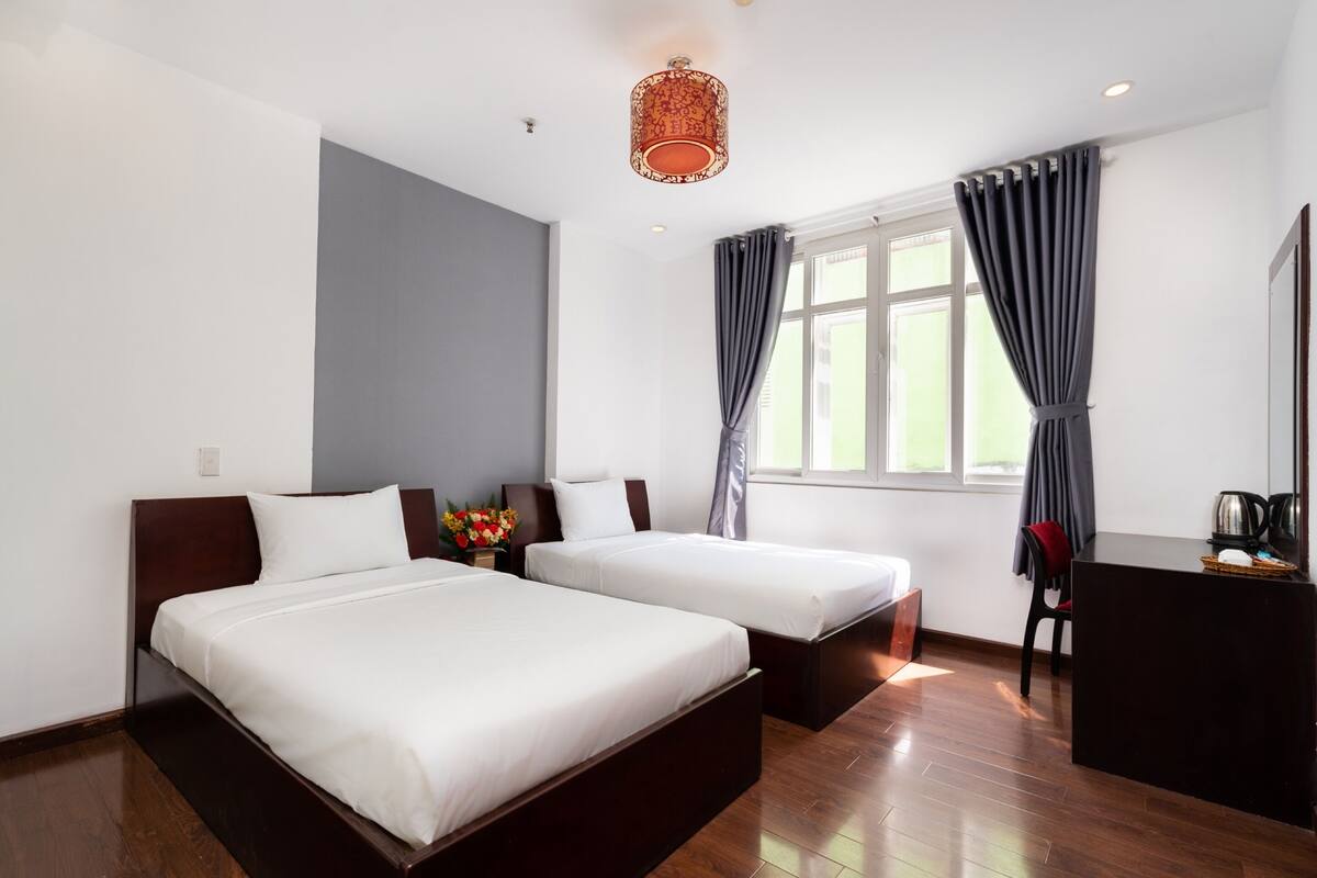 A hotel room with two single beds, a desk, a chair, a coffee maker, and a window with curtains.