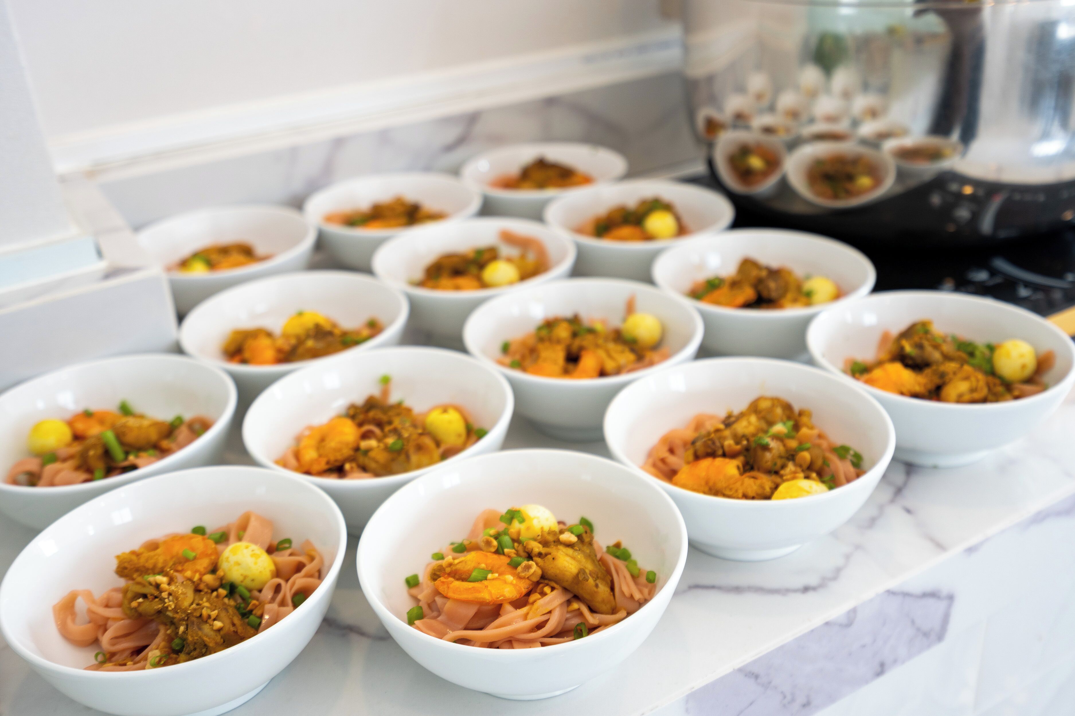 A series of white bowls containing various dishes, arranged on a marble countertop.