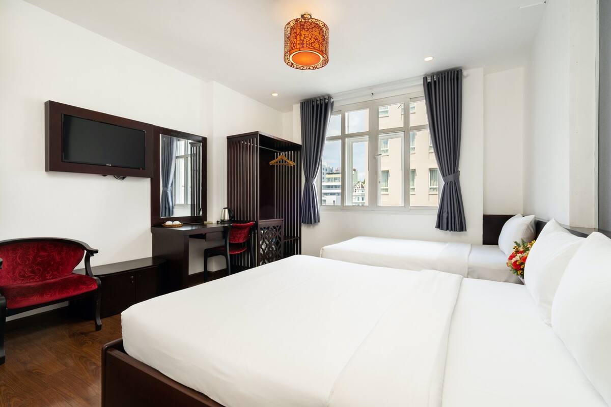 A hotel room with a bed, a desk, a chair, a TV, and a window with curtains.