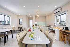A modern hotel dining area with a long table, chairs, and a view of the city through large windows.