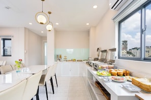 Un espace repas moderne avec une longue table, des chaises et un buffet proposant divers plats.