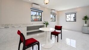 A modern hotel lobby with a marble reception desk, two red upholstered chairs, a white round table, and large windows offering city views. -  A&A Toronto Hotel (Ho Chi Minh City)
