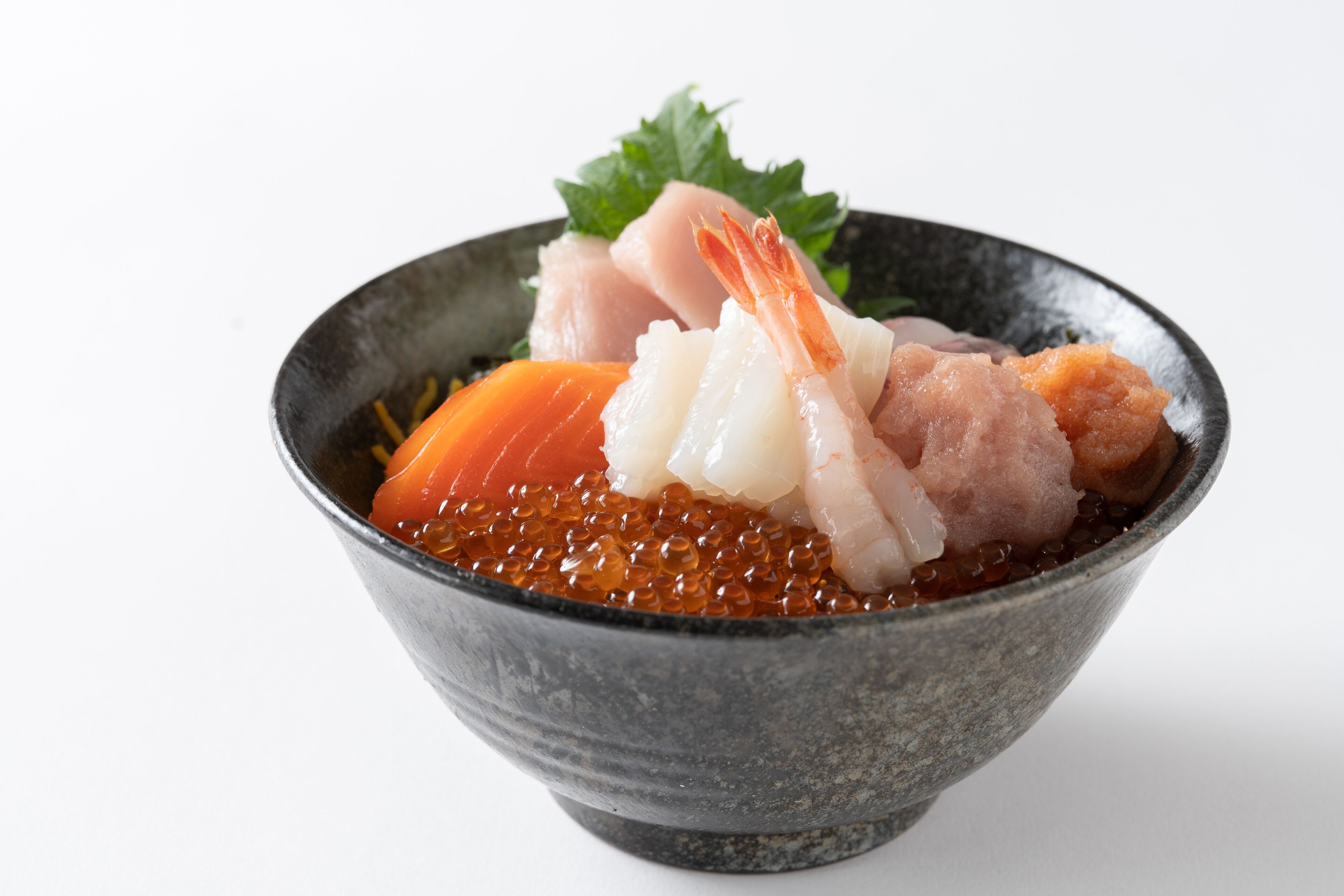 A bowl of sushi with various toppings including fish, shrimp, and salmon roe.