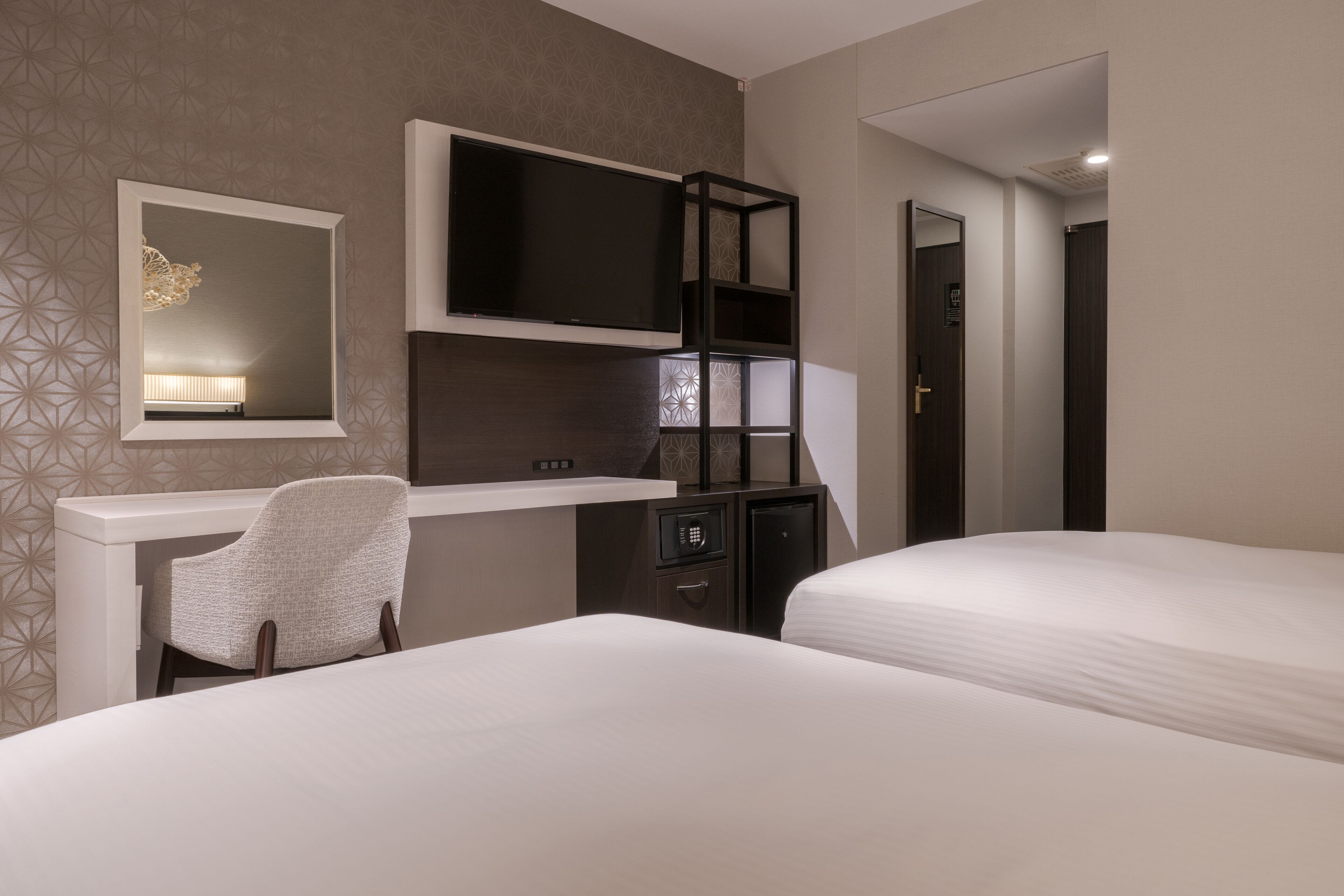 A hotel room with two beds, a desk with a chair, a TV, and a wardrobe.