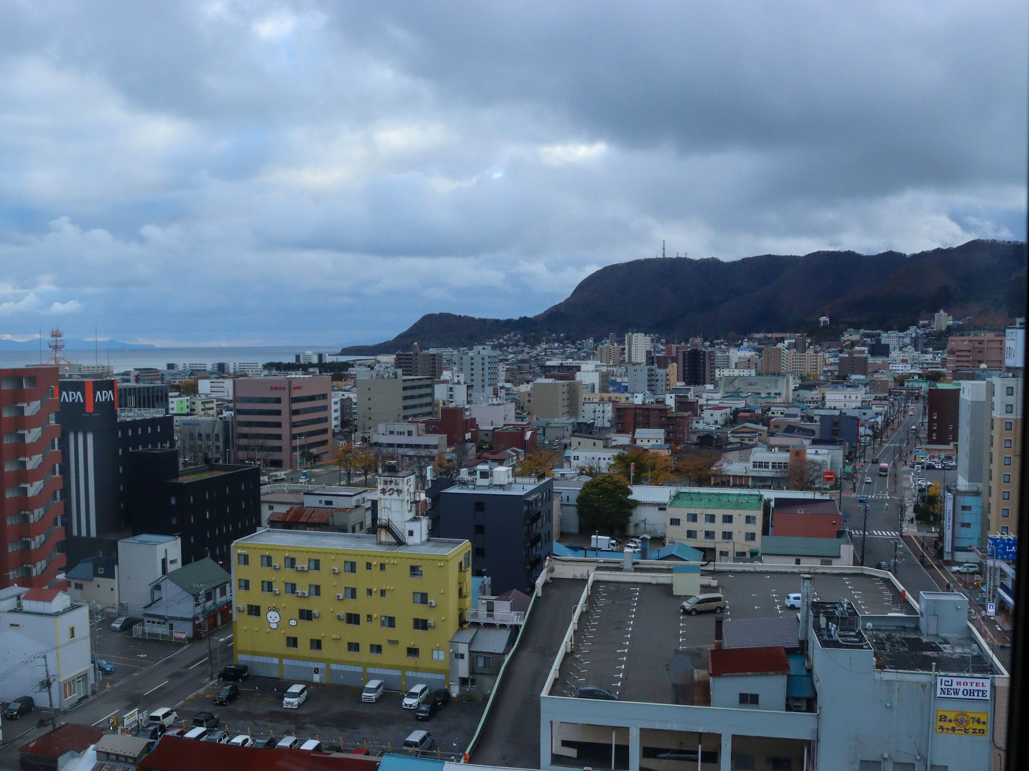 A cityscape with a prominent yellow building in the foreground, a variety of other buildings, and a mountain in the background.
