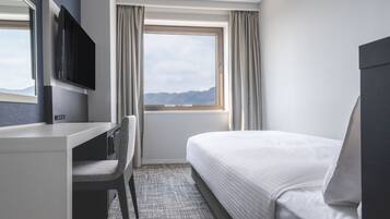 A hotel room with a bed, a desk, a chair, a TV, and a window with curtains.