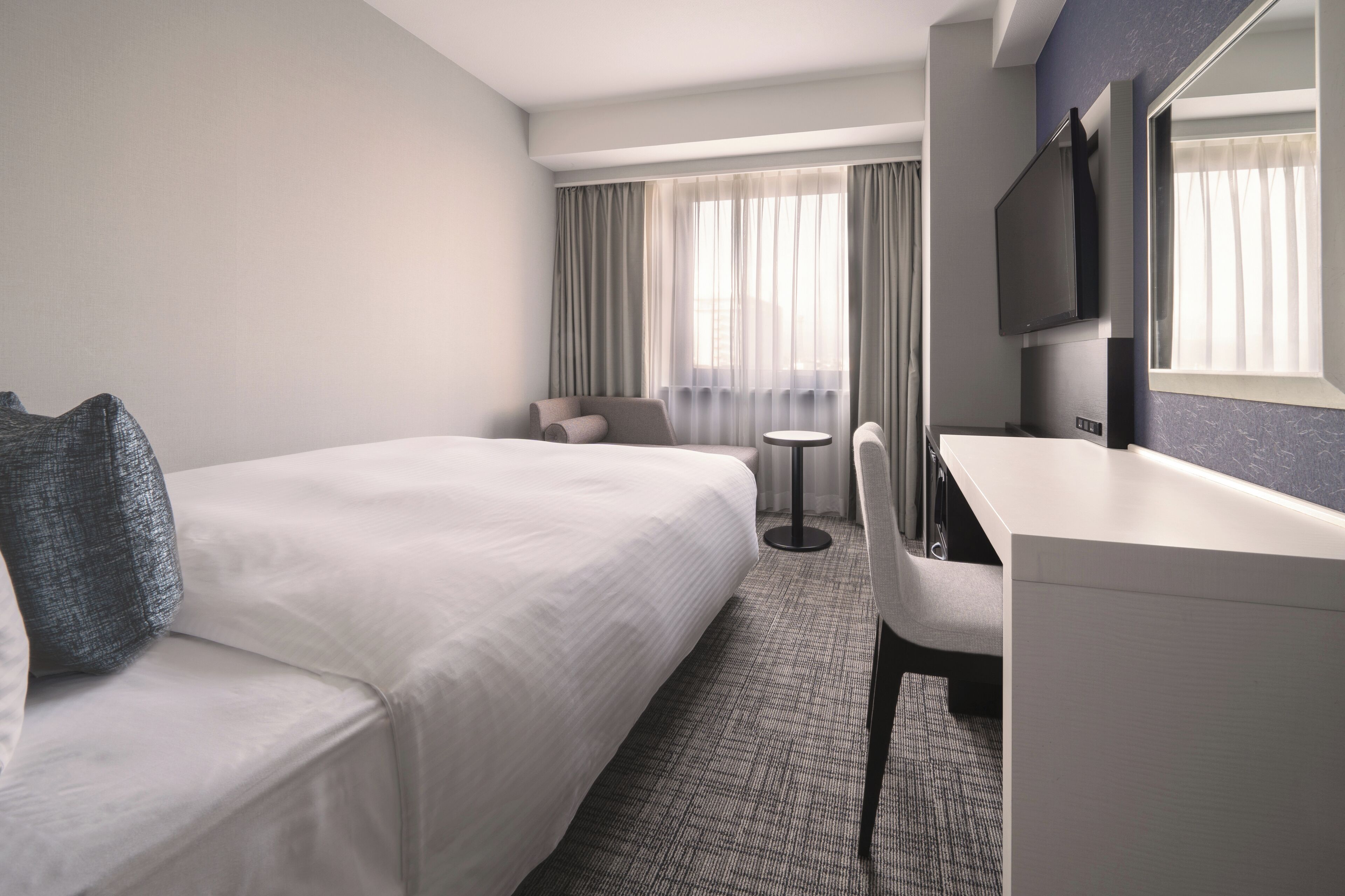 Une chambre d’hôtel avec un lit, un bureau, une chaise et un téléviseur.