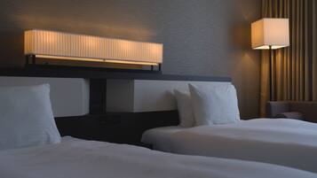 A hotel room with two beds, a headboard with integrated lighting, a bedside table, and a wall-mounted lamp.