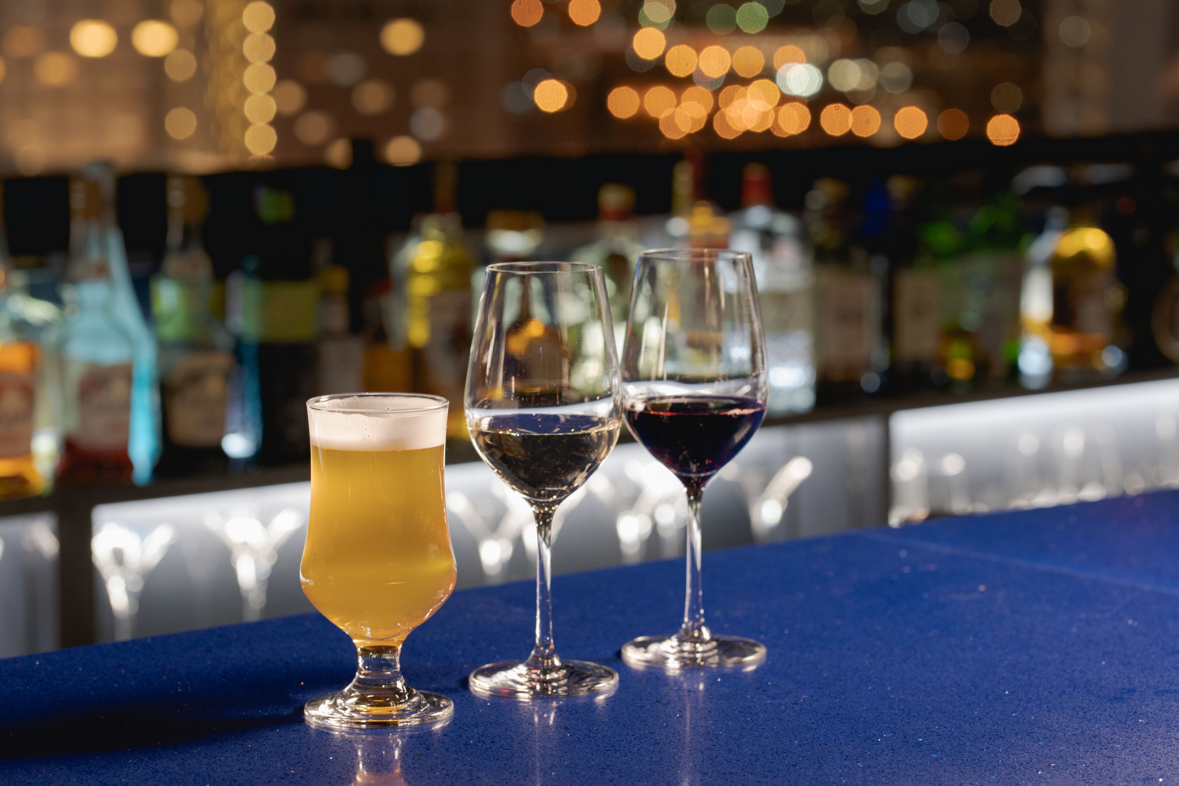 Trois verres contenant différentes boissons sont posés sur le comptoir d’un bar, avec un arrière-plan flou composé de bouteilles.