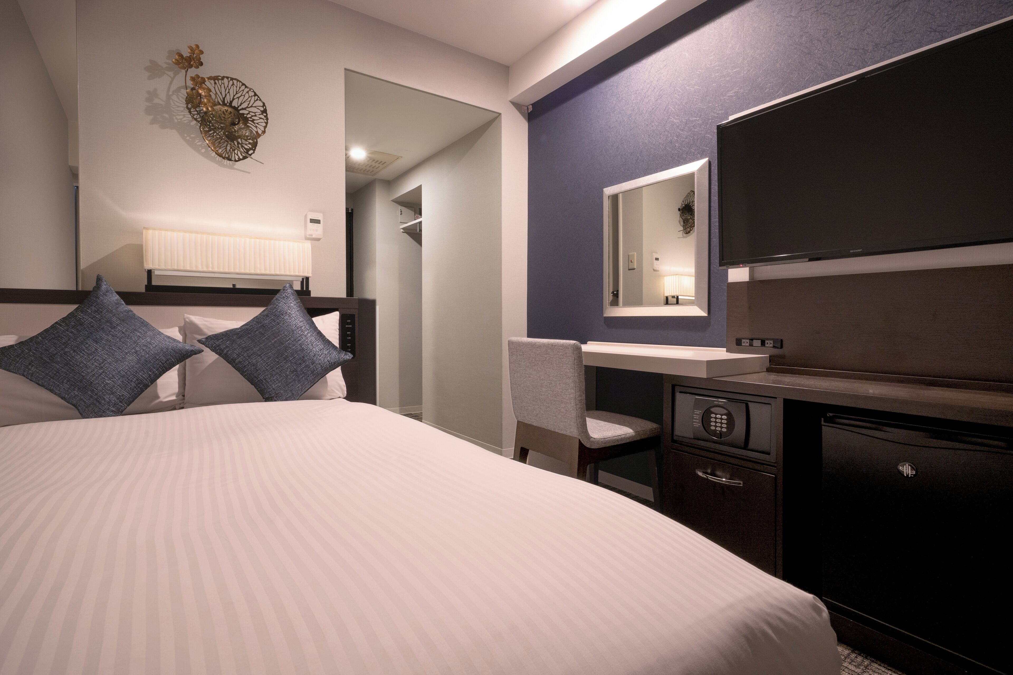 Una habitación de hotel con cama, escritorio, silla, televisión y minibar.