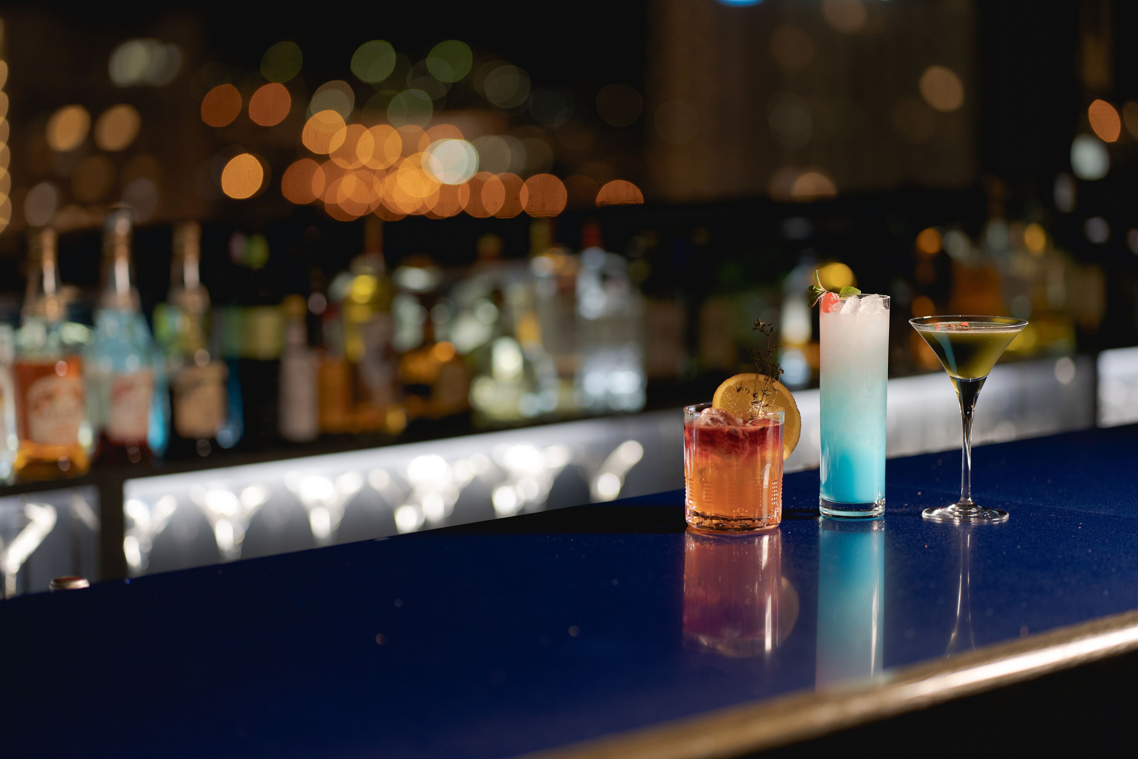 Una barra con tres bebidas, una botella de licor y una copa de martini.