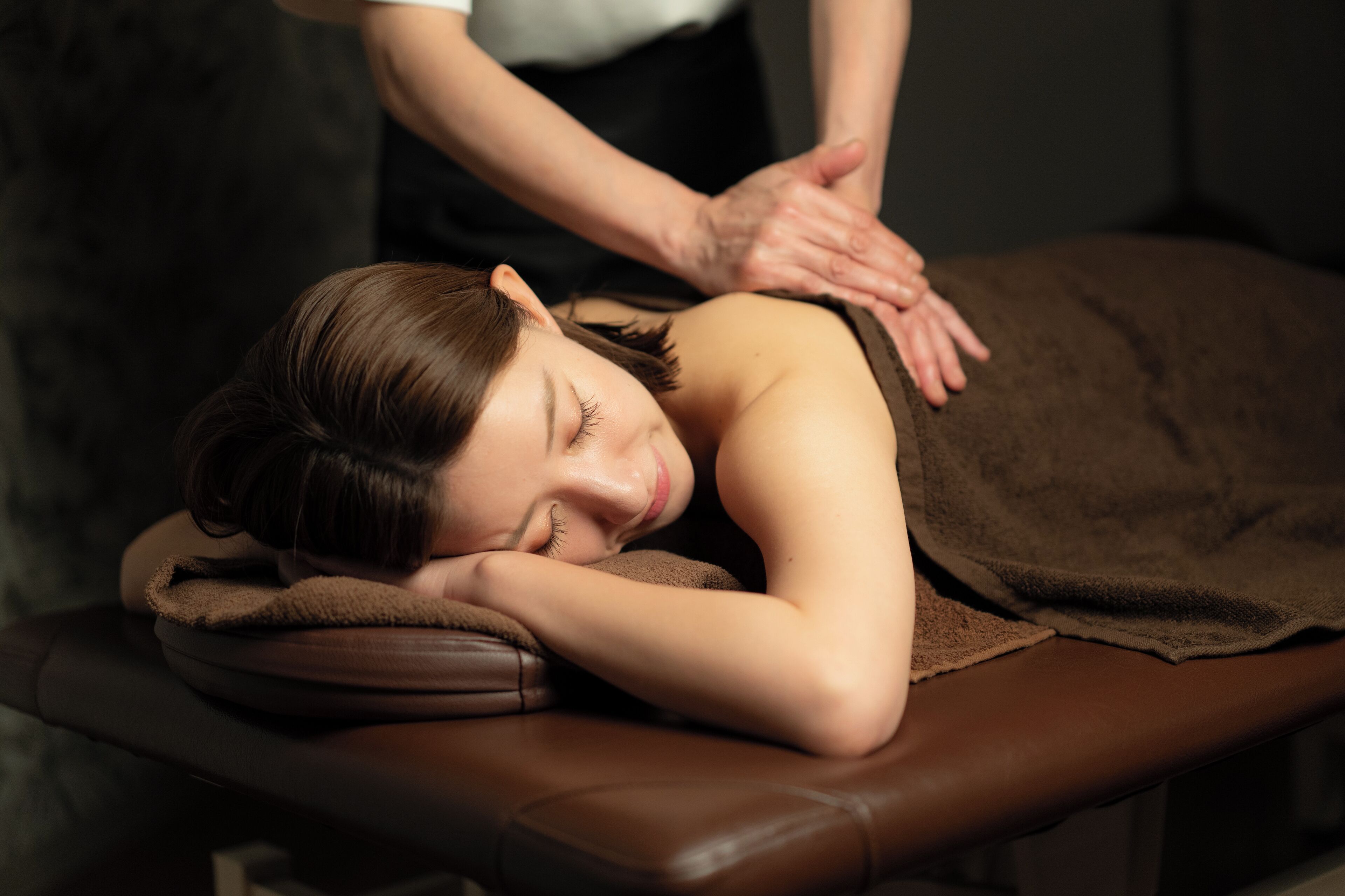 A person lying on a massage table with a brown towel covering them.