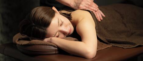 A person lying on a massage table with a brown towel covering them.
