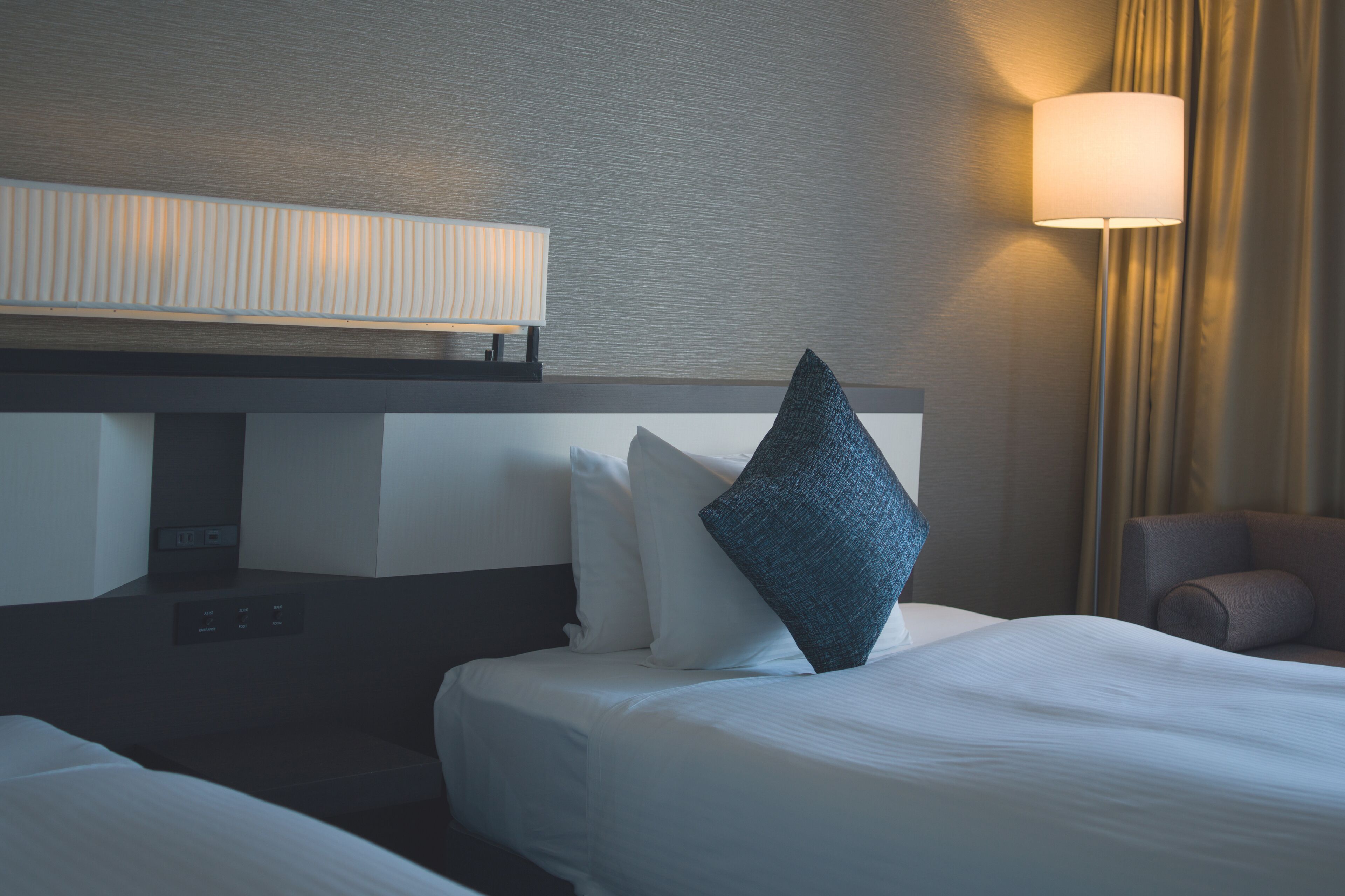 A hotel room with a bed, a control panel, a lamp, and a chair.