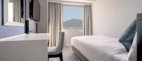 Habitación de hotel con cama, escritorio, silla, televisor y ventana con cortinas.