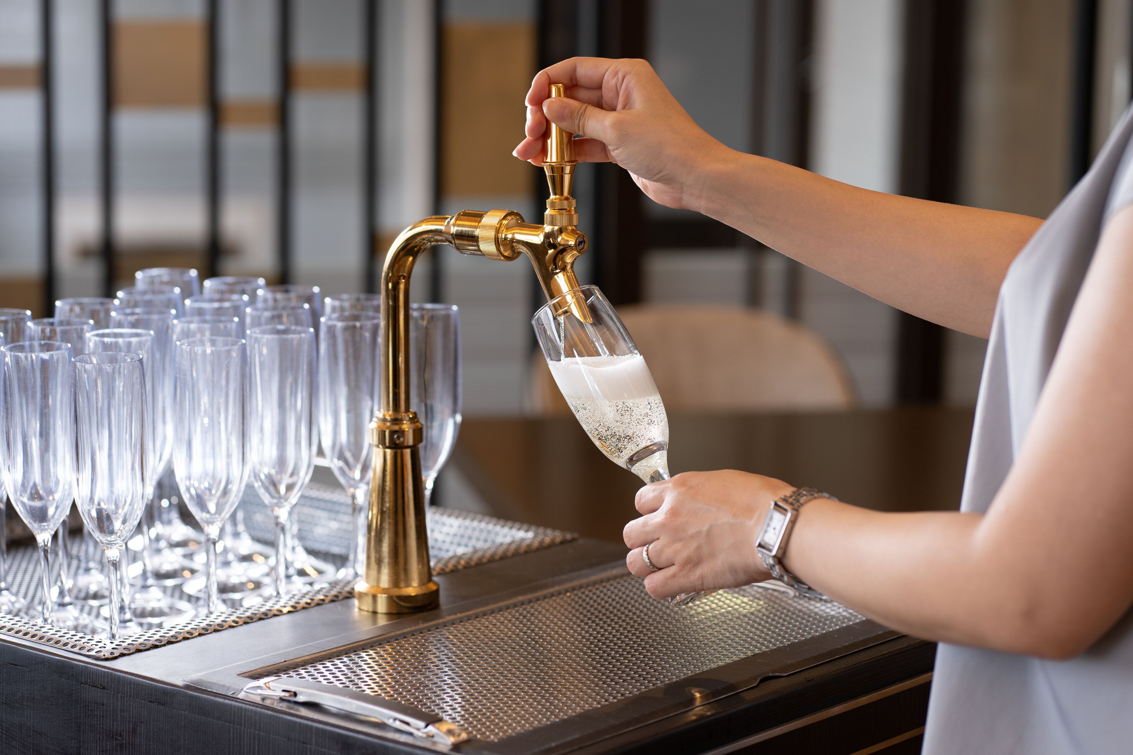 A person pouring champagne into a glass from a gold tap.