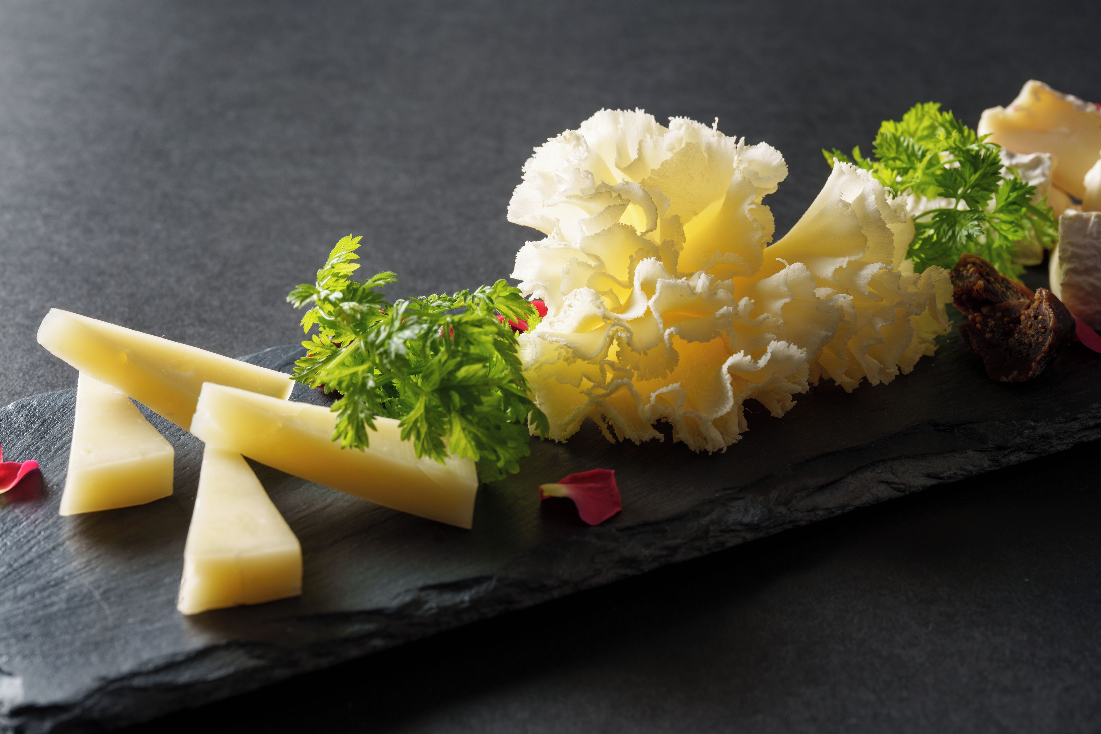 A cheese board with various cheeses and garnishes on a slate board.