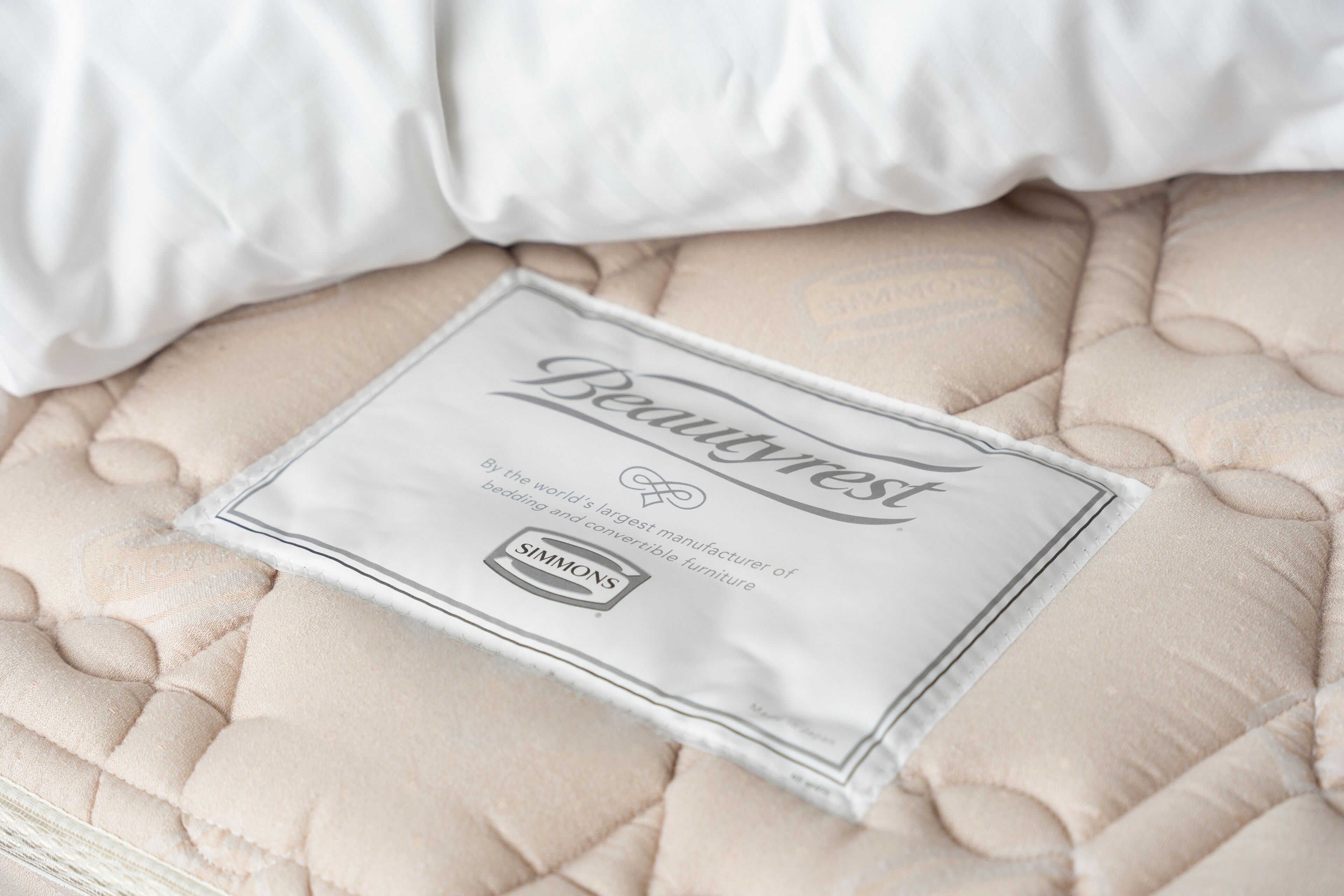 Een beige geborduurde spreidekbed met een kussen en een etiket waarop 