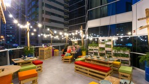 Un área de comedor al aire libre con mobiliario de madera y luces colgantes.