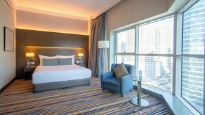 Habitación de hotel con una cama grande, una silla, una mesita y una ventana con vistas a la ciudad.