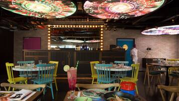 Un restaurante con sillas y mesas de colores, un techo decorativo grande y una pared de ladrillo.