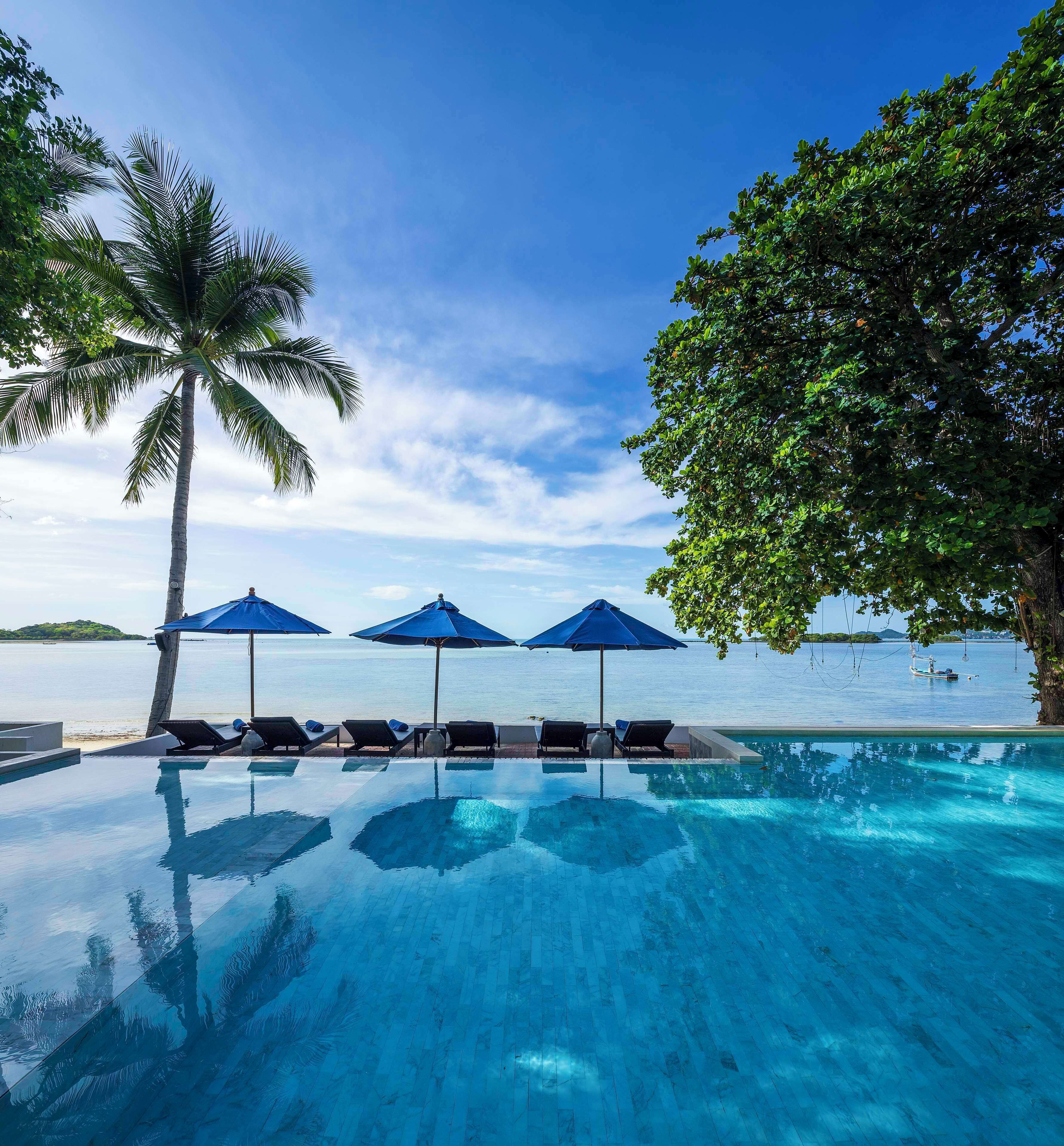 An infinity pool with lounge chairs and umbrellas, overlooking a calm sea and a clear sky.