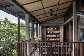 A covered outdoor seating area with a bookshelf and a ceiling fan. - Homm Chura Samui (Koh Samui)