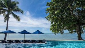 A poolside area with lounge chairs and umbrellas, overlooking a body of water. - Homm Chura Samui (Koh Samui)