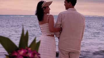Una pareja de pie junto a una mesa, con vista al mar, una vela y un vaso de agua.