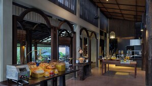 A spacious indoor area with multiple tables set up for dining, featuring various food items and a coffee machine. - Homm Chura Samui (Koh Samui)