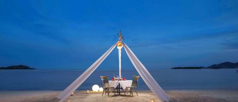 A beachside dining setup with a table and chairs, a canopy, and candles.