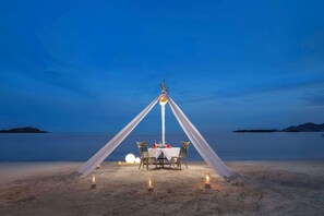 A beachside dining setup with a table and chairs, a canopy, and candles. - Homm Chura Samui (Koh Samui)