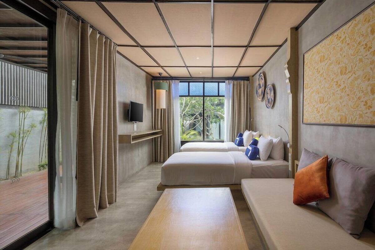 A modern hotel room with two beds, a sofa, a TV, and a large window with curtains.