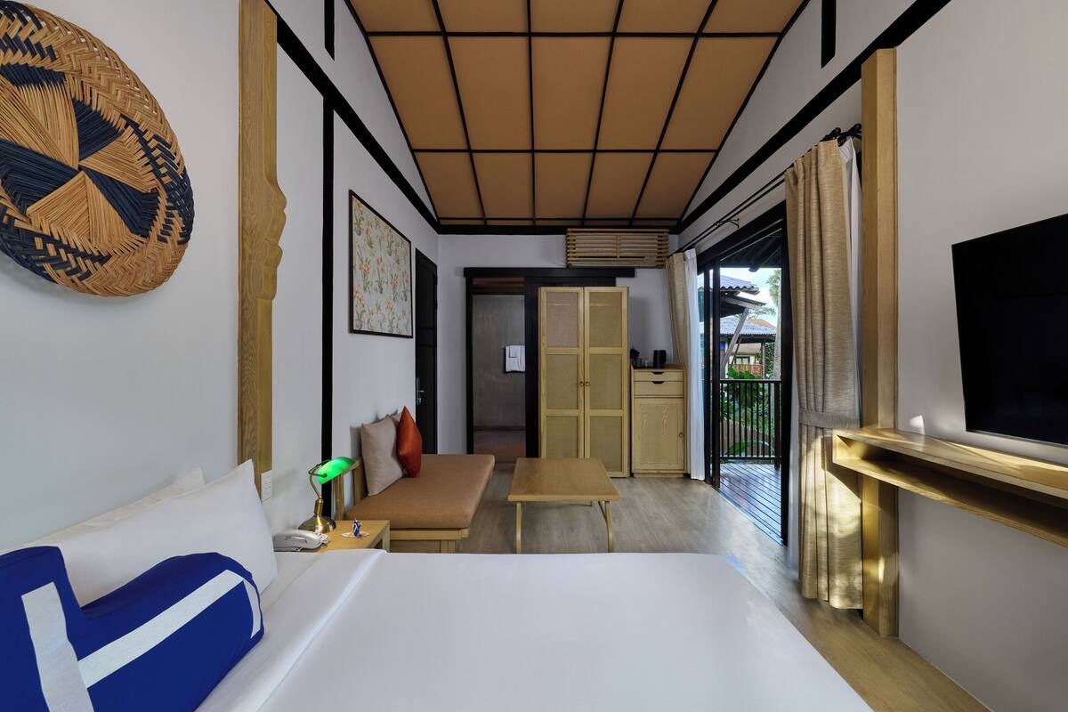 A hotel room with a bed, a desk, a sofa, a television, a window, and a door leading to a balcony.