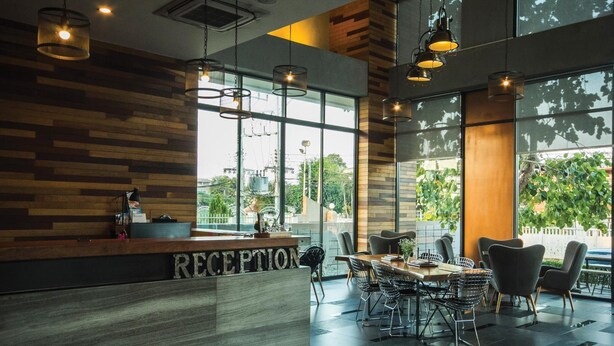 A reception area with a wooden reception desk, modern chairs, and large windows offering a view of the outdoors. - Space 59 Ratchaburi (Ratchaburi)