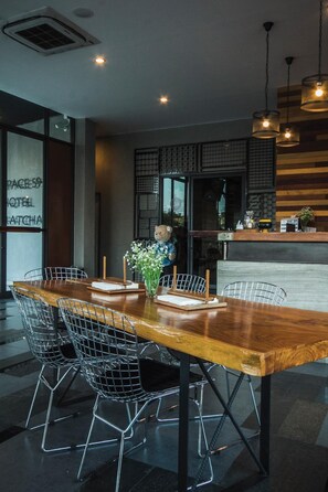 A modern dining area with a wooden table and wire mesh chairs, a vase with flowers, and a wooden counter with a cash register.