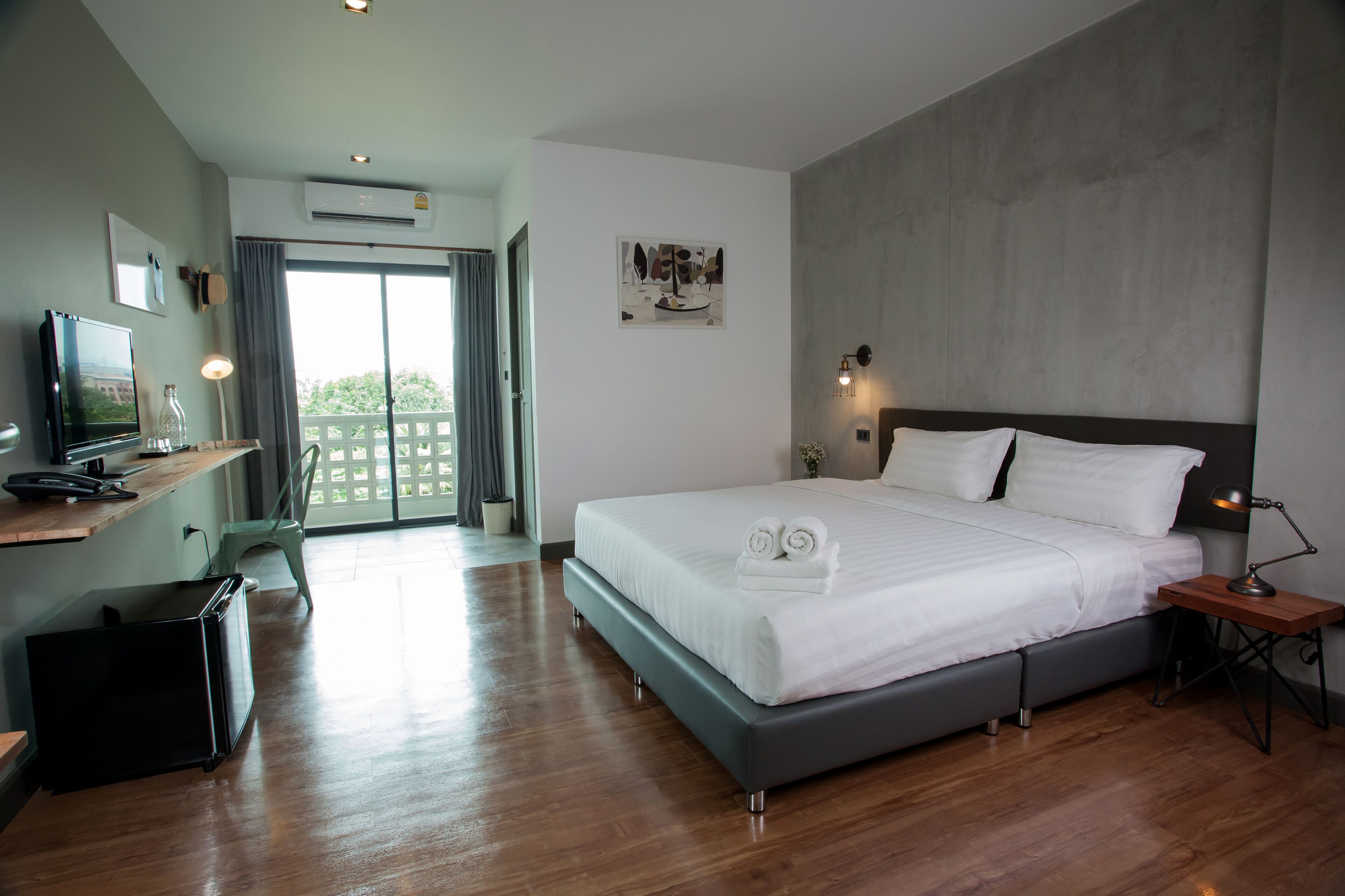 A modern hotel room with a large bed, a desk with a computer, a flat-screen TV, and a balcony with a view.