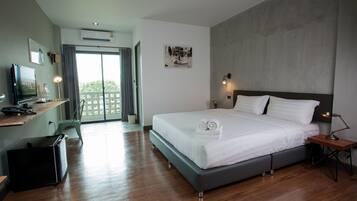 A modern hotel room with a large bed, a desk with a computer, a flat-screen TV, and a balcony with a view.