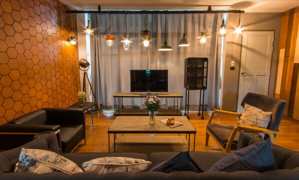 A modern living room with a sofa, armchairs, a coffee table with flowers, a TV, and pendant lights.