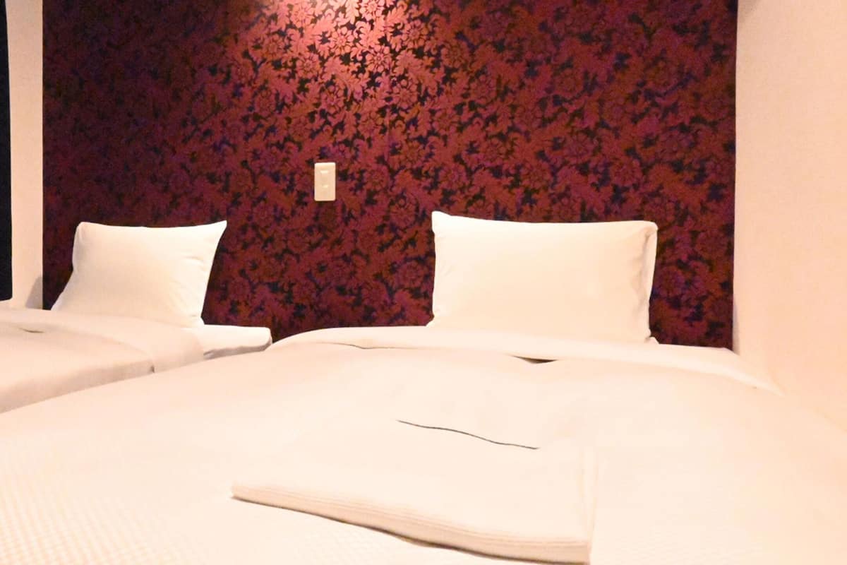 Camera d'albergo con due letti, entrambi con lenzuola e cuscini bianchi, e una parete decorata con un motivo floreale.
